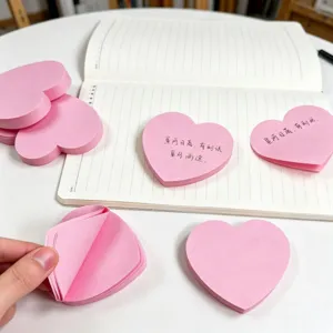 Gros plan de notes adhésives roses en forme de cœur avec texte manuscrit sur un bureau propre.