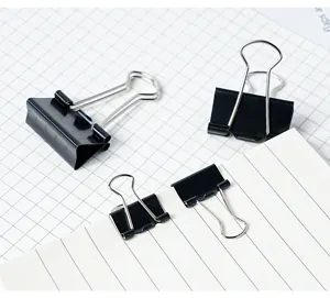 Gros plan de pinces à relier métalliques noires de différentes tailles sur papier quadrillé.