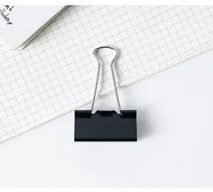 Gros plan d'une pince à relier en métal noir sur papier quadrillé pour documents de bureau.