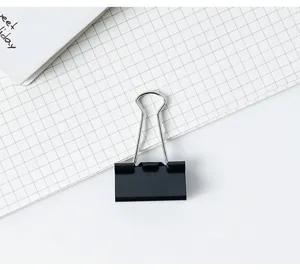 Gros plan d'une pince à relier métallique noire sur papier quadrillé pour bureau et école.