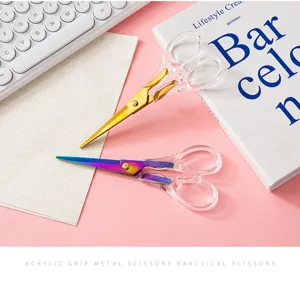 Close-up detail of clear acrylic handle scissors with metallic gradient blades in lifestyle setup.