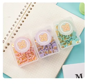 Nahaufnahme von bunten Macaron-Pinnnadeln in transparenten Schachteln mit süßem Bären auf Tisch.