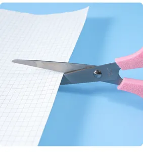 Nahaufnahme Detailansicht von rosa Macaron Schreibwaren Schere schneidet Gitterpapier.