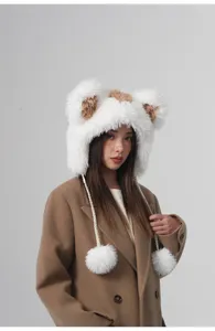 Detailansicht der flauschigen Bärenohrenmütze in Weiß und Braun mit weichen Pompons