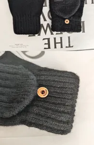 Detalle de guantes calefactables de punto negro con botón de madera y solapa.