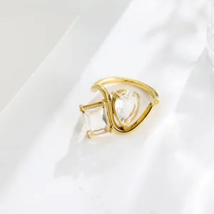 Close-up of asymmetrical twin crystal ring with emerald and pear cut stones in gold finish.