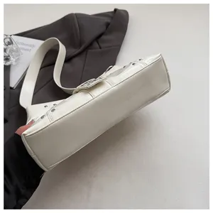 Close-up of cream punk style underarm bag with silver rivets and metallic buckle.