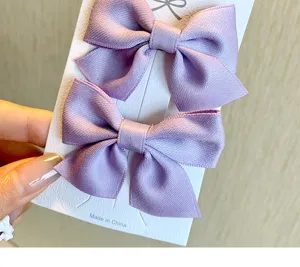 Dettaglio di due graziose mollette per capelli a fiocco viola chiaro su carta bianca.