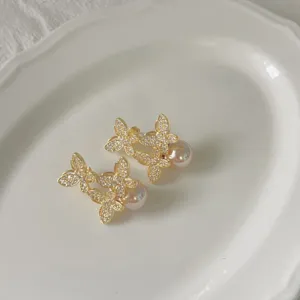 Detailopname van gouden vlinder zirkonia parel oorknopjes op een wit keramisch bordje.