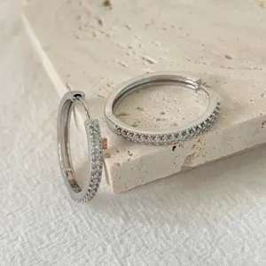 Primo piano dettagliato di eleganti orecchini a cerchio in zircone su superficie in pietra.