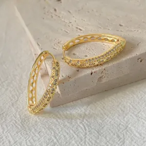Primo piano dettagliato di orecchini a cerchio dorati traforati con zirconi lucidi.