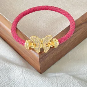 Nahaufnahme eines rosa geflochtenen Lederarmbands mit einer goldenen Zirkonia Schmetterlingsschnalle.