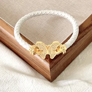 Weißes geflochtenes Lederarmband mit goldenem Schmetterlingsverschluss und funkelnden Strasssteinen.