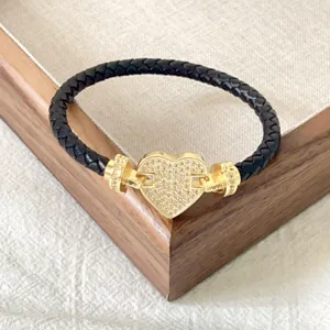 Primo piano del bracciale in pelle nera intrecciata con chiusura a cuore dorata.