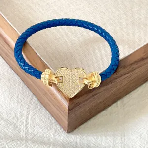 Dettaglio del bracciale in pelle intrecciata blu con ciondolo a cuore dorato e chiusura.