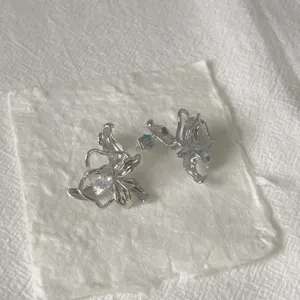 Primo piano di orecchini a lobo floreali 3D irregolari in metallo con cristalli.