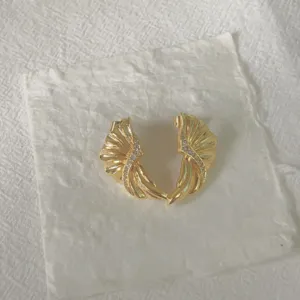 Nahaufnahme von vergoldeten muschelformigen Ohrringen mit funkelnden Zirkoniasteinen detail.