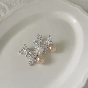 Detailopname van sprankelende zirkonia vlinder parel oorbellen op een witte keramische schaal.