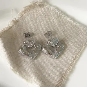 Close-up of silver-plated heart stud earrings with sparkling micro-set cubic zirconia details.
