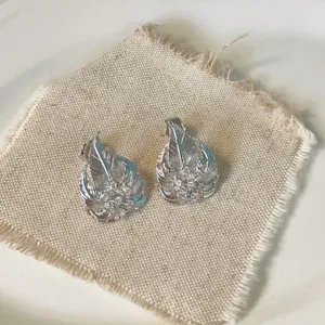 Primo piano di eleganti orecchini argentati a forma di foglia con zirconi scintillanti.