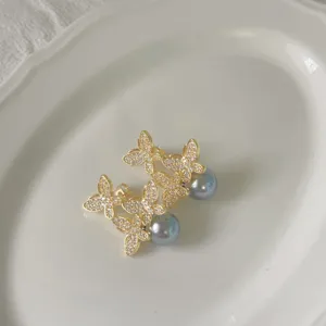 Detail van gouden vlinder parel oorbellen met sprankelende zirkonia op witte schaal.