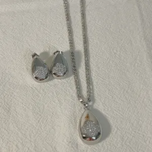 Detailed view of silver teardrop pendant necklace and matching earrings set with pave cubic zirconia.