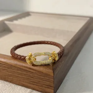 Brown braided leather bracelet detail featuring a gold-toned micro-paved crystal horseshoe clasp.
