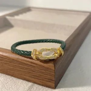 Green braided leather bracelet detail featuring a gold micro paved horseshoe buckle clasp.