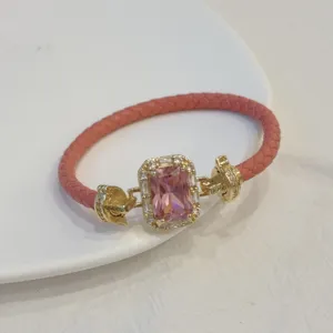Dettaglio di bracciale in pelle intrecciata rosa con chiusura dorata in zircone quadrato.