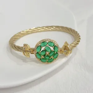 Detailed shot of gold-plated twisted cable bracelet with green zirconia round cluster clasp.