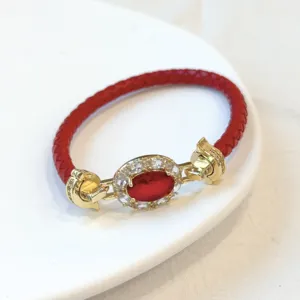 Dettaglio di un bracciale in pelle intrecciata rossa con zirconi e finiture in metallo dorato di lusso.