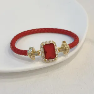 Primo piano del bracciale in pelle rossa con pietra rettangolare dorata e zirconi brillanti.