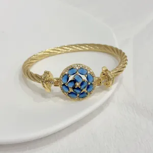 Detailed close-up of a gold-plated cable twist bangle with a sparkling blue zircon floral center.