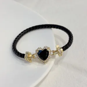 Close-up of black braided leather bracelet with gold-plated black heart zircon crystal clasp.
