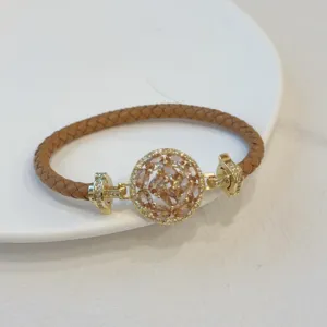 Close-up detail of a braided brown leather bracelet featuring an 18k gold plated round clasp.