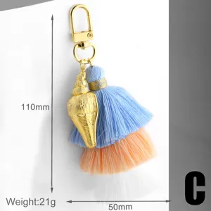 Close-up detail of the colorful cotton tassel and golden shell keychain charm accessory.