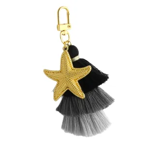 Porte-clés étoile de mer dorée avec pompon dégradé noir et gris, charm de sac élégant.