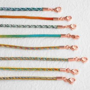 Close-up detail of colorful braided necklace cords with rose gold clasps and metal tips.