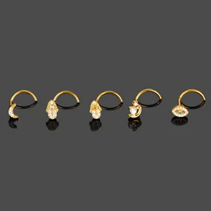Detail view of gold titanium nose stud rings featuring moon hamsa and evil eye charms.