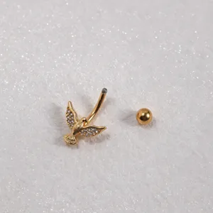 Primo piano dettagliato di un piercing da ombelico dorato alato con zirconi scintillanti.