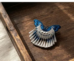 Detailed closeup of ethnic embroidered butterfly tassel hair clip, traditional Miao style metal accessory.