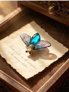 Close-up detail of vintage gradient cicada wing insect brooch with blue crystal body in wooden box.