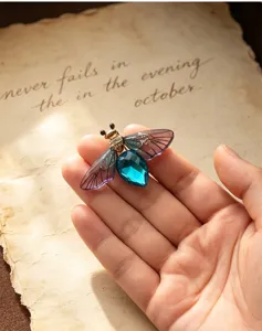 Close-up detail of the vintage crystal bee brooch featuring translucent gradient wings in hand.