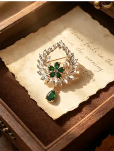 Vintage emerald wreath brooch with rhinestones and teardrop pendant for elegant attire.