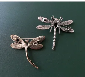 Detailed view of the back structure of two vintage dragonfly brooches, showing secure pin closures.