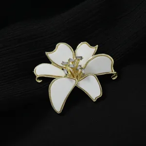 Nahaufnahme der eleganten weissen Blumenbrosche mit goldenem Rand und Kristalldetails.