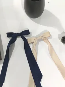Dettaglio di due eleganti fermagli a fiocco in raso con nastri lunghi in blu navy e beige
