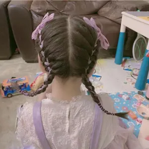 Detailansicht von geflochtenem Haar eines Mädchens mit lila Schleifen-Haarspangen zu Hause.