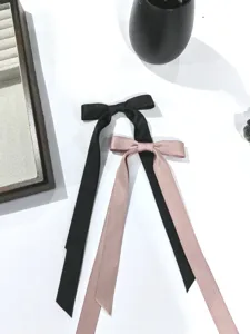 Dettaglio di eleganti mollette per capelli con fiocco a nastro lungo in raso nero e rosa