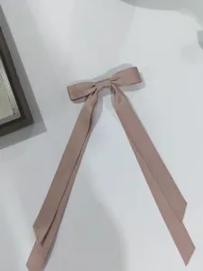 Dettaglio di una molletta per capelli a doppio fiocco rosa con lunghi nastri.